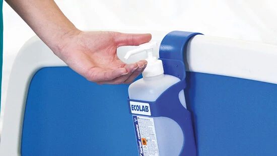 Hand reaching for a wall-mounted Ecolab hand sanitizer dispenser on a blue and white surface.